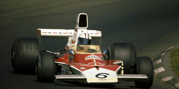 A vintage McLaren Formula 1 car with number 6 and Texas sponsorship is racing on a track, approaching a corner at the Rolex Motorsport Reunion.