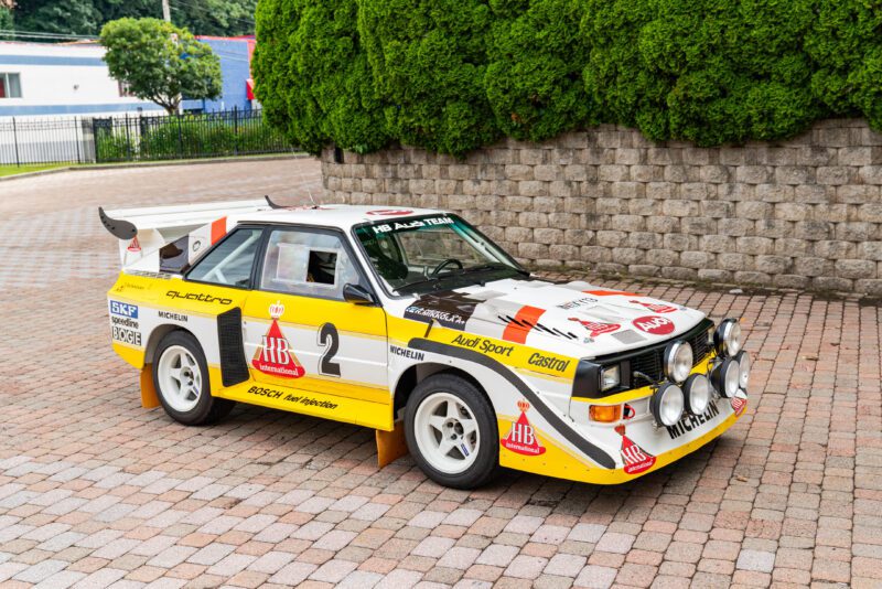 Audi Quattro rally car with number 2 and sponsor decals, parked on a brick surface by a stone wall and greenery—one of the 2025 Bonhams Monterey: 10 Must-See Cars Crossing the Block at The Quail.