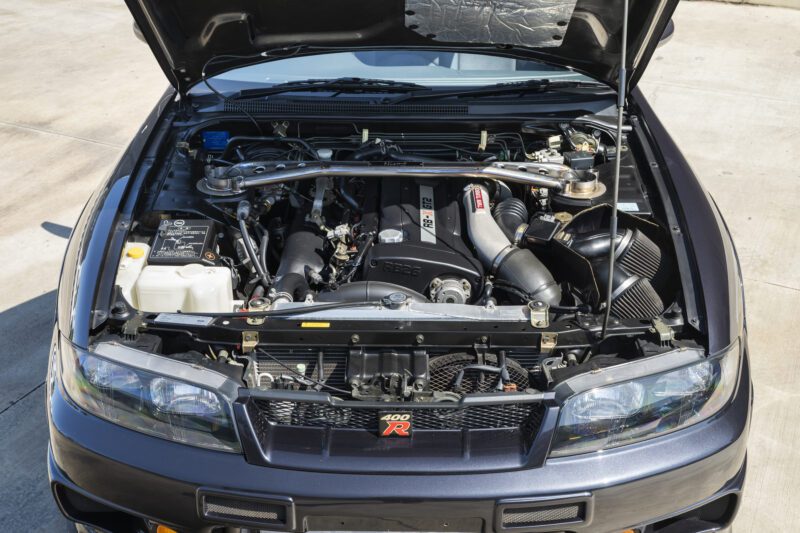 An ultra-rare Nissan Skyline GT-R R33 NISMO 400R with its hood open, showcasing a detailed view of the RB26DETT engine and various meticulously maintained engine bay components.