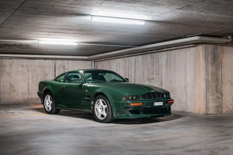 A dark green 90s sports car is parked in a concrete underground parking garage under fluorescent lights, evoking nostalgia for classic cars and the history of automotive design.
