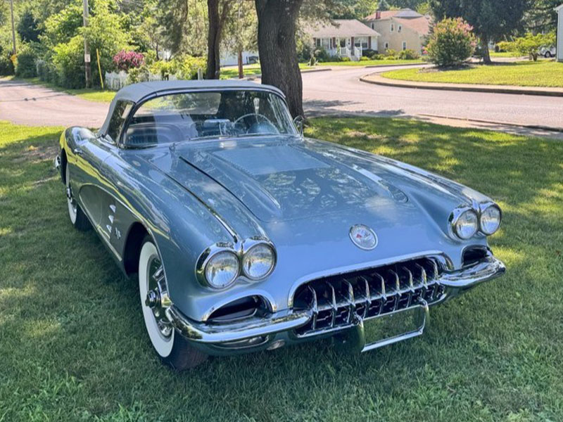 A light blue vintage convertible with whitewall tires is parked on grass near a tree in a suburban neighborhood, looking ready for the Fall Carlisle Collector Car Auction or any true collector car enthusiast.