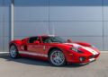 A red Ford GT sports car with white racing stripes, one of the best 2000s cars, is parked on a paved surface in front of a gray building.