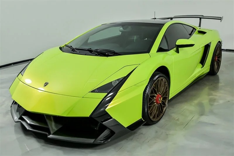 A lime green V10 supercar with black accents and a large rear wing, this Lamborghini Gallardo is photographed in a showroom with a plain background and is now available for sale.