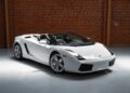 A white Lamborghini Gallardo convertible V10 supercar is parked indoors on a polished floor in front of a brick wall.