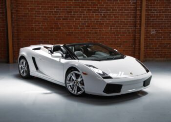 A white Lamborghini Gallardo convertible V10 supercar is parked indoors on a polished floor in front of a brick wall.