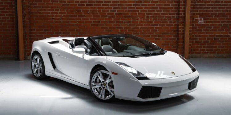 A white Lamborghini Gallardo convertible V10 supercar is parked indoors on a polished floor in front of a brick wall.