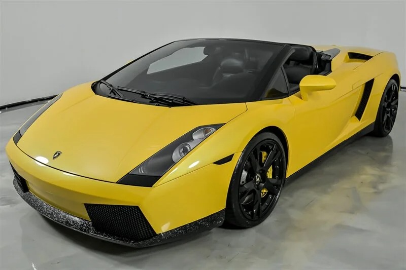 A yellow Lamborghini Gallardo Spyder convertible V10 supercar with black wheels is parked indoors on a glossy floor.