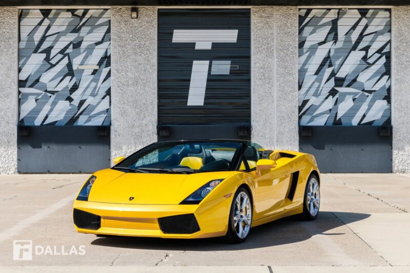 A yellow V10 supercar, this Lamborghini Gallardo Spyder convertible is parked in front of a building with geometric-patterned garage doors.