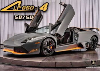 A grey Lamborghini Murciélago LP 650-4 with its scissor doors open sits on a turntable, showcasing orange accents and #50-of-50: LAST Lamborghini Murciélago LP 650-4 Roadster for Sale at Prestige Imports special edition branding.