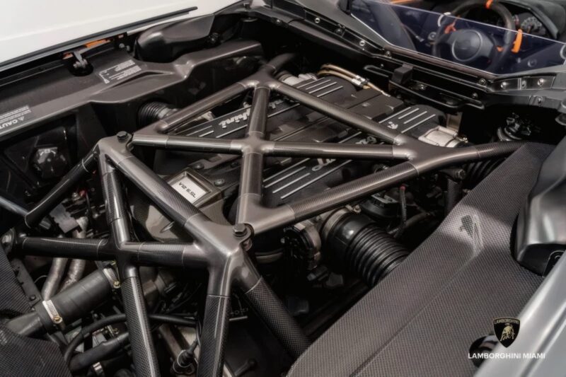 Close-up view of a Lamborghini engine bay, featuring carbon fiber cross brace and Lamborghini Miami branding. Showcased is the #50-of-50: LAST Lamborghini Murcielago LP 650-4 Roadster for Sale at Prestige Imports.