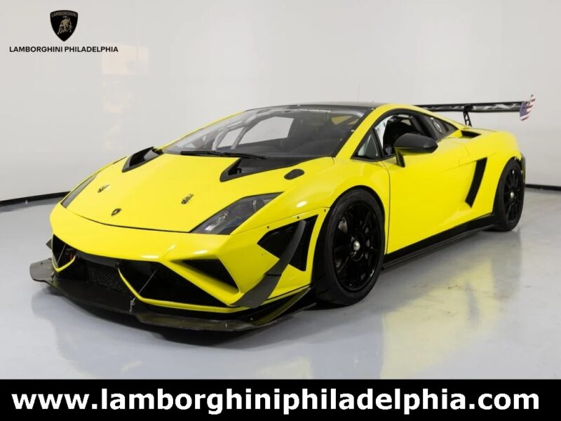A yellow Lamborghini Gallardo V10 supercar with black accents is displayed in a showroom, featuring the Lamborghini Philadelphia logo and website—perfect for those seeking exclusive Lamborghini Gallardos for sale.