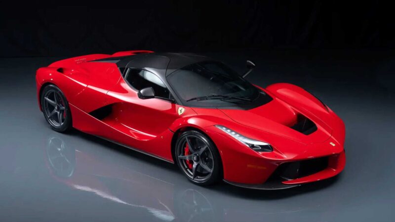 A red Ferrari LaFerrari hybrid sports car with black accents is parked on a glossy gray floor against a dark background, reminiscent of the stunning showcases at the 2025 RM Sotheby's Monterey Auction: Top 10 Results And Highlights.
