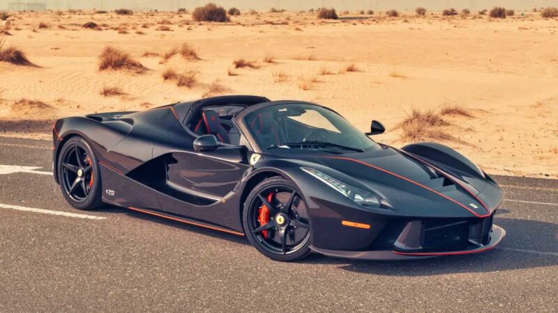 A black Ferrari LaFerrari Aperta with red accents is parked on an empty road against a sandy desert backdrop, reminiscent of standout entries at the 2025 RM Sotheby's Monterey Auction: Top 10 Results And Highlights.