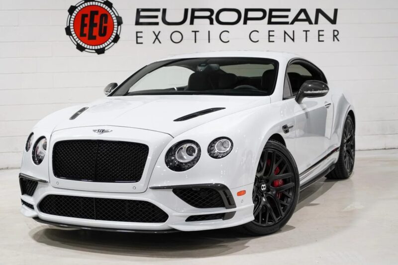 A white Bentley Continental GT, the ultimate luxury tourer, with sleek black accents is parked indoors in front of a European Exotic Center sign.