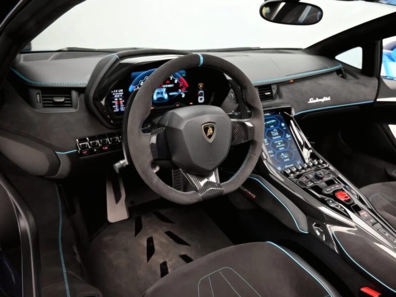 Interior of a Lamborghini Centenario Roadster—only 10 in the U.S.—showing the steering wheel, digital dashboard, center console with touch controls, and black upholstery with blue accents.