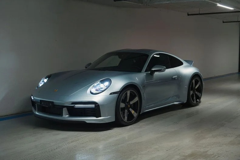 A silver Porsche 911 Sport Classic is parked indoors under artificial lighting, facing slightly to the left—a modern nod to Porsche history and timeless design.
