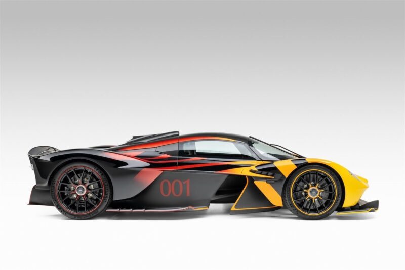An ultra-rare Aston Martin Valkyrie sports car in black, red, and yellow with the number 001 on the door, shown in side profile against a plain white background.
