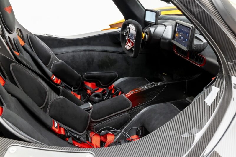 Ultra-rare Aston Martin Valkyrie for sale: View of a sports car interior featuring two bucket seats with red harnesses, a digital dashboard, a central control panel, and carbon fiber detailing.