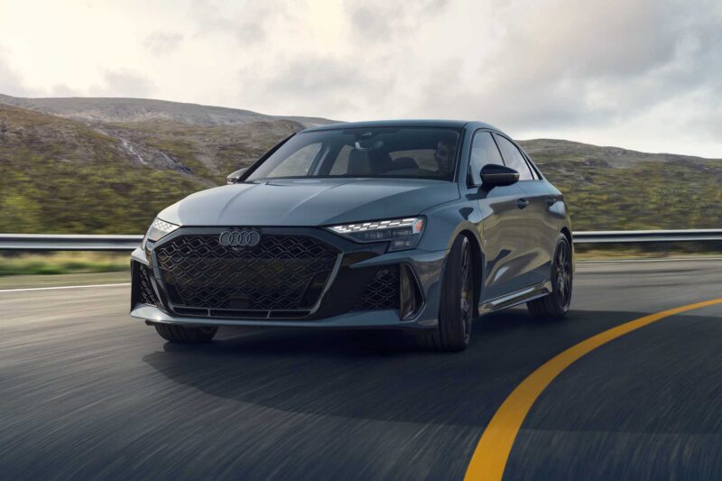 A gray Audi sedan—The Last Surviving 5-Cylinder On Sale Today Packs A Punch—as it drives on a winding road, mountains and clouds forming a dramatic backdrop.
