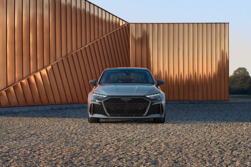 A silver Audi car is parked on a cobblestone surface in front of a modern copper-paneled building, showcasing The Last Surviving 5-Cylinder On Sale Today Packs A Punch from the front view.