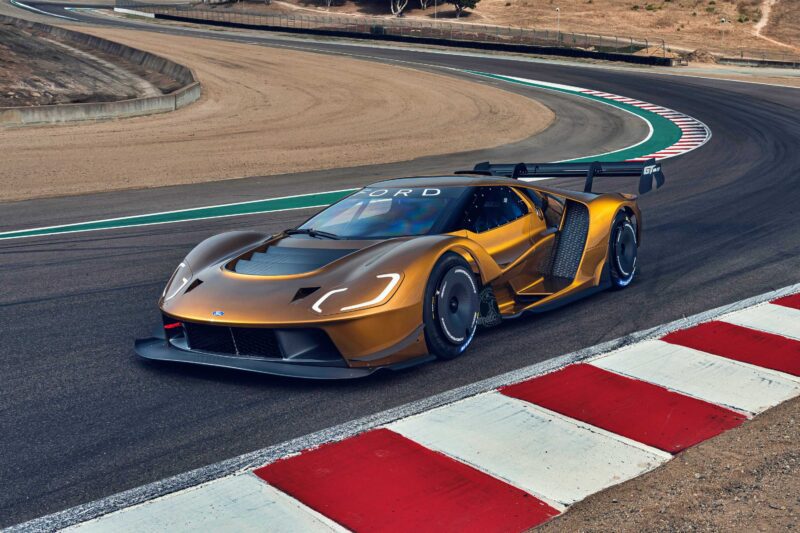 A gold Ford GT Mk IV race car with aerodynamic features speeds along a curving racetrack with red and white curbs, celebrating the Ford Performance Launches Final Production Run of the legendary model.