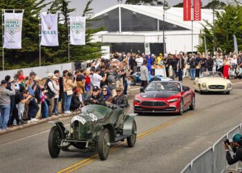 A parade of classic and modern cars, including Silver Arrows Hollywood Cars and Concept Cars: Mercedes’ Pebble Beach Highlights, drives past cheering spectators at an outdoor auto event, with banners and tents visible in the background.