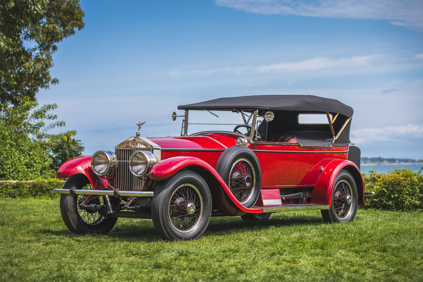 A vintage red convertible car with black soft top roof parked on grass, featuring classic round headlights and spoked wheels, shines at the 15th Anniversary Misselwood Concours d’Elegance, drawing record attendance.