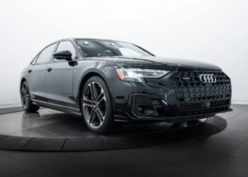 A black Audi luxury car is displayed in a showroom with a white background, shown from a front-side angle on a rotating platform.