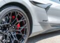 Close-up of a 2025 Corvette ZR1 C8's front wheel, featuring black rims, red brake calipers, and a carbon fiber trim detail on the white body. For Sale.