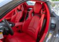 Red leather interior of a 2025 Corvette with two bucket seats, center console, and visible door featuring warning labels. For sale and ready to impress.