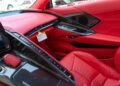 The image shows the red leather interior of a 2025 Corvette ZR1 C8 sports car, featuring carbon fiber accents, control buttons, display screen, and passenger seat—an impressive luxury vehicle currently for sale.