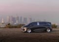 A futuristic black Mercedes-Benz Vision V concept van, exuding luxury, is parked on an empty lot with the city skyline visible in the background under a hazy sky.
