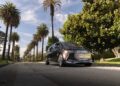 A futuristic, silver Mercedes-Benz Vision V concept van luxury electric car is parked on a palm tree-lined residential street under a partly cloudy sky.