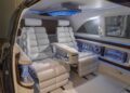 The Mercedes-Benz Vision V concept features a futuristic car interior with two white, cushioned seats, LED accent lighting, a central armrest, and a minibar with bottled drinks built into the side panel for true van luxury.