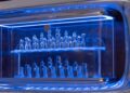 A glass chess set displayed on two shelves inside a blue-lit refrigerator, evoking the concept of van luxury found in the Mercedes-Benz Vision V.