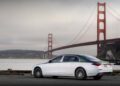 A white and green Mercedes-Maybach S 680 luxury sedan, part of the limited edition Emerald Isle series, is parked near the water with the Golden Gate Bridge in the background on a cloudy day.