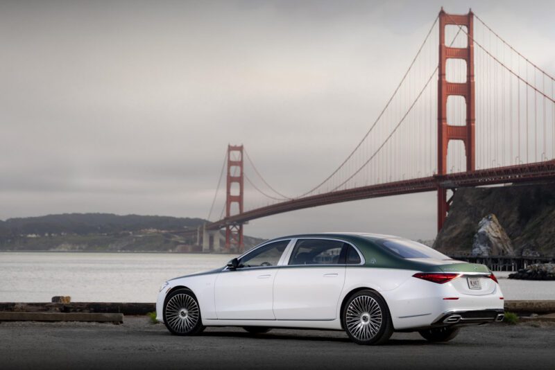 A white and green Mercedes-Maybach S 680 luxury sedan, part of the limited edition Emerald Isle series, is parked near the water with the Golden Gate Bridge in the background on a cloudy day.