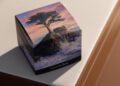 A box with an image of a tree on a rocky island and the words "Upon Emerald Isle" and "Mercedes-Benz" sits on a beige leather surface, hinting at a limited edition inspired by the elegance of the Mercedes-Maybach S 680.