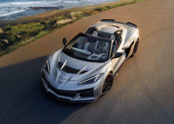 A Quail Silver Limited Edition Corvette ZR1X convertible is parked on a paved road near the coastline, with the ocean and greenery visible in the background, evoking the exclusive vibe of Monterey Car Week.