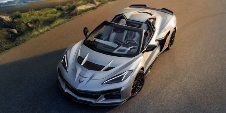 A Quail Silver Limited Edition Corvette ZR1X convertible is parked on a paved road near the coastline, with the ocean and greenery visible in the background, evoking the exclusive vibe of Monterey Car Week.