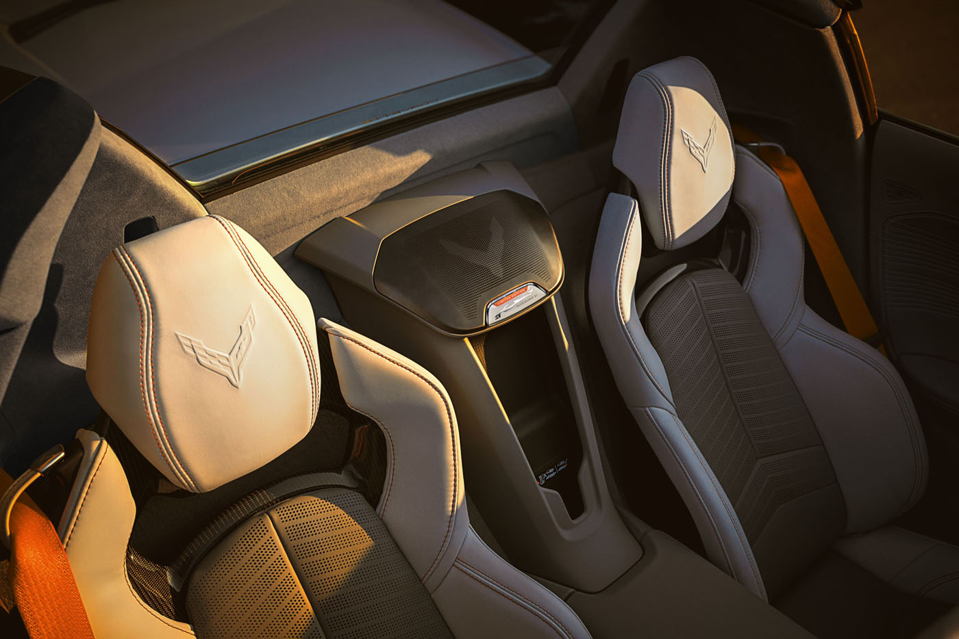 Close-up view of two light-colored leather car seats with Corvette logos and orange seat belts in a convertible, possibly from the Quail Silver Limited Edition showcased at Monterey Car Week.