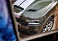 A green 2026 Dodge Durango Hellcat Jailbreak with white racing stripes is seen from above through a window, showcasing the front hood, grille, and left headlight—one of 6 million possible builds with an incredible 710 HP.