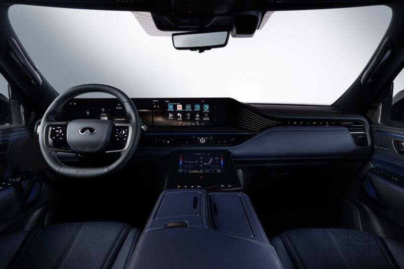 View of a modern vehicle interior featuring a digital dashboard, steering wheel with logo, touchscreen controls, and premium materials in dark colors—the 2026 INFINITI QX80 introduces SPORT Grade and ups the luxury game.