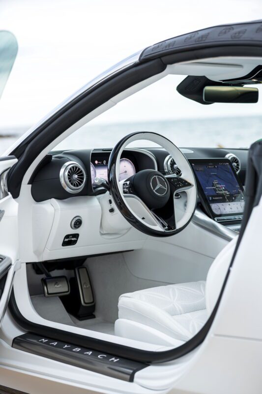 Close-up view of the interior of a luxury Maybach, featuring a modern dashboard, digital displays, and white leather seats that blend sporty elegance with ultimate comfort.