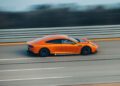 An orange AMG GT speeds down a multi-lane road, its blurred background hinting at thrilling motion—perfect for an epic journey like Around The World In 8 Days.