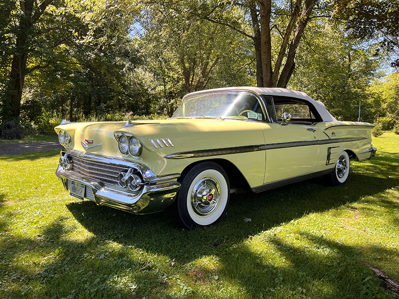 A vintage yellow convertible car with a black soft top is parked on grass under trees on a sunny day, ready to shine at the Fall Carlisle Collector Car Auction in October 2025 among other six star cars.