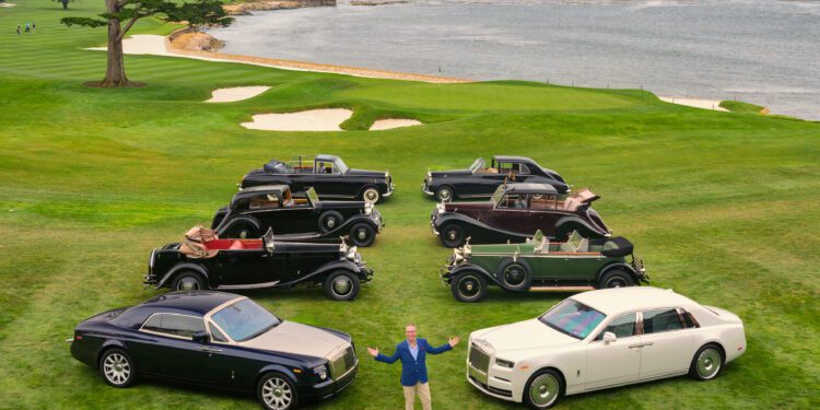 A man stands on a golf course at Pebble Beach in front of vintage and modern Rolls-Royce Phantom cars, celebrating 100 Years of automotive excellence against a stunning coastal landscape.