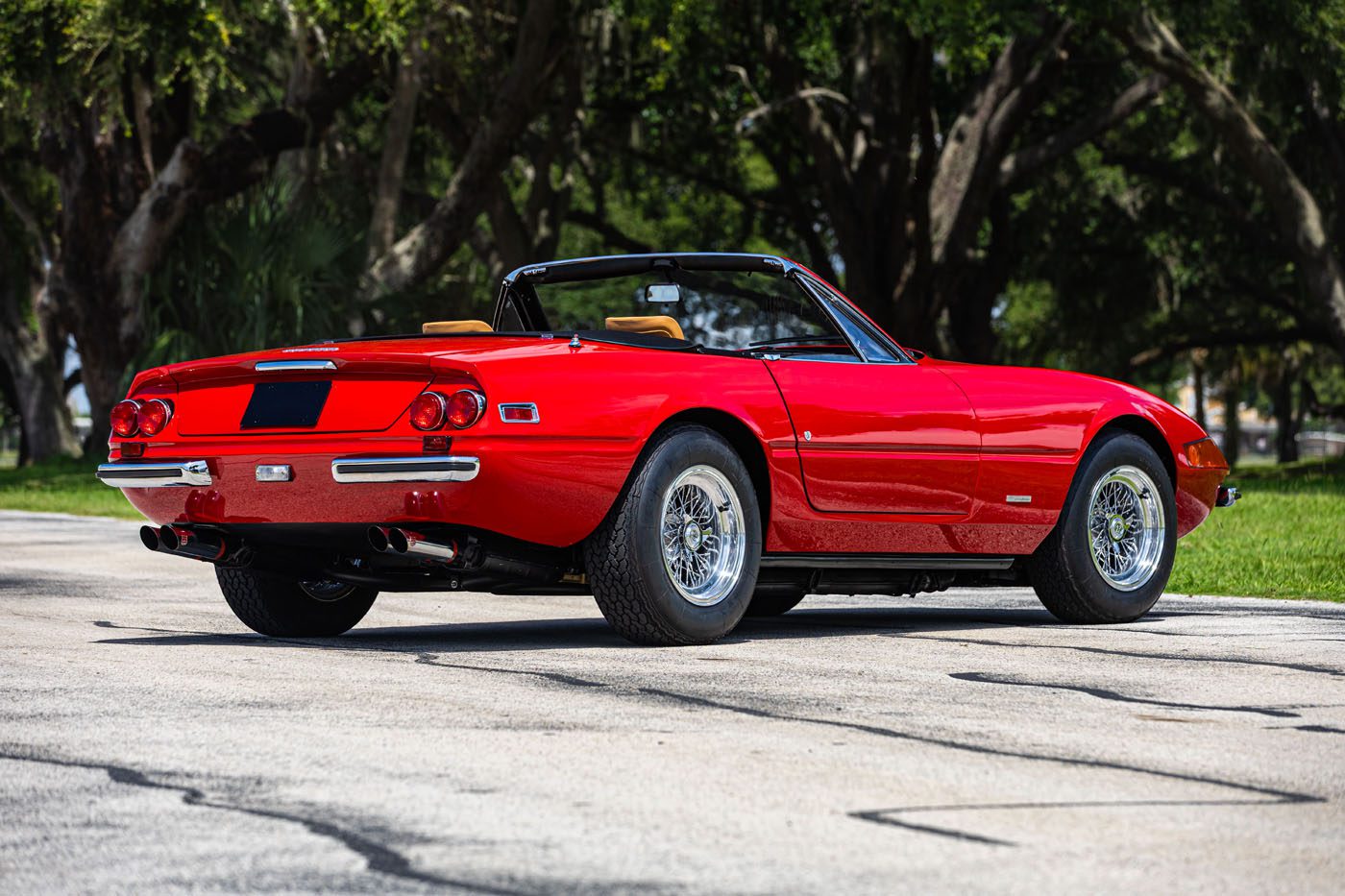 A classic red convertible sports car with the top down is parked on a paved road, surrounded by grass and trees—perfect for Ferrari Legends fans heading to Monterey 2025 or the next Mecum Auction.