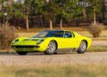 A bright yellow Lamborghini Miura sports car, a true million-dollar car, is parked on a paved road with grass, bushes, and trees in the background—ready to turn heads at the Monterey 2025 Auction by Mecum.