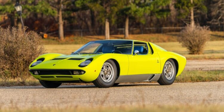 A bright yellow Lamborghini Miura sports car, a true million-dollar car, is parked on a paved road with grass, bushes, and trees in the background—ready to turn heads at the Monterey 2025 Auction by Mecum.
